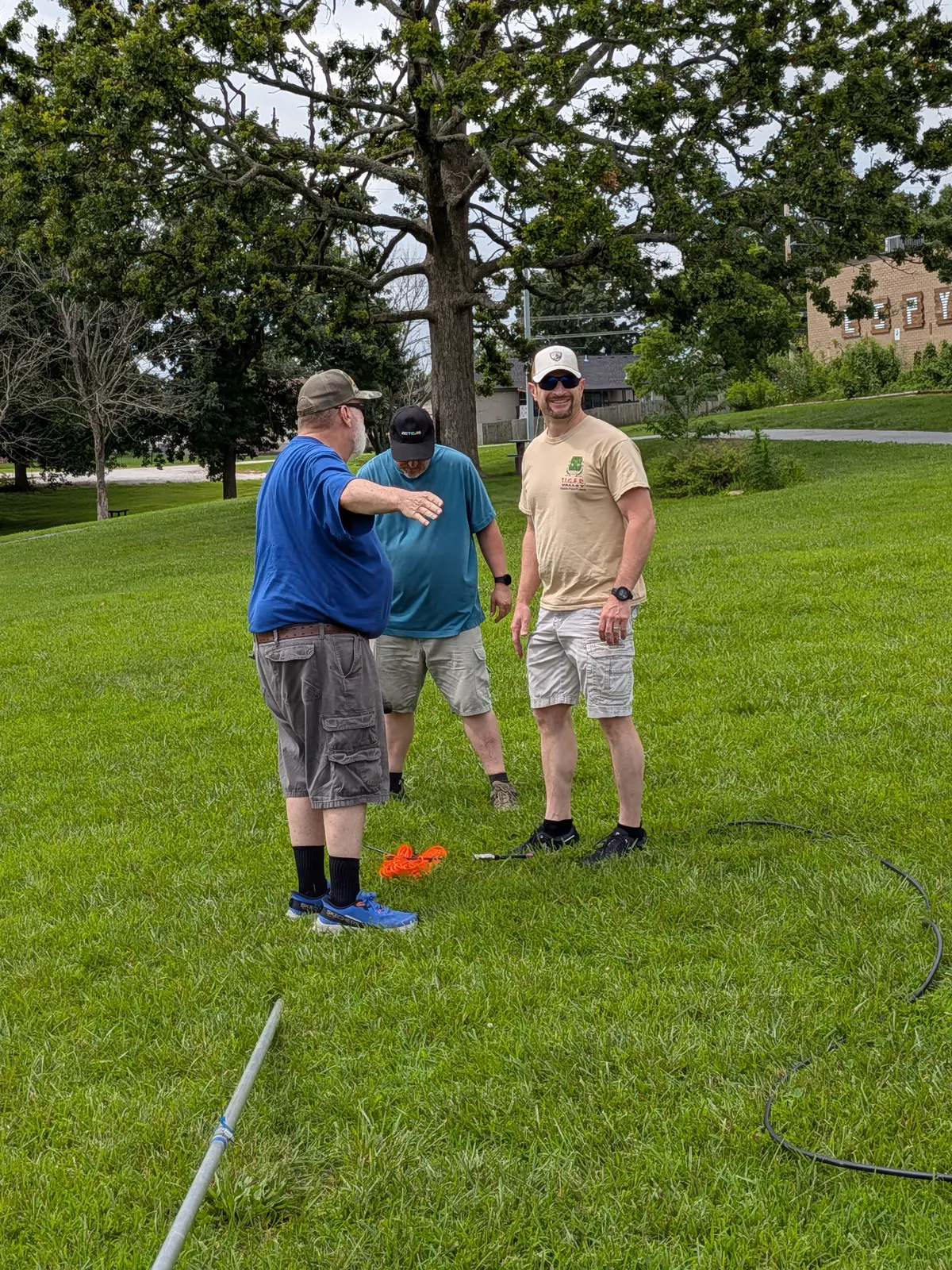Three club members laying out coax and raising an antenna in a park.